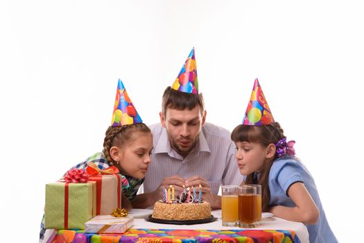 Dad and two daughters together blow out the candles on the cake