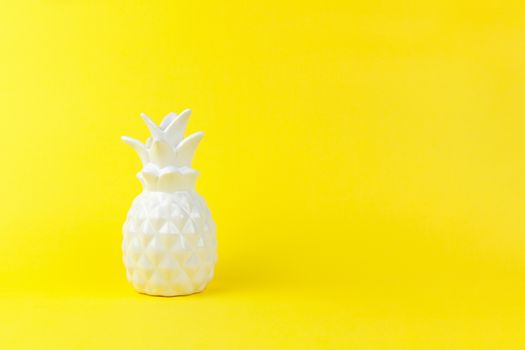 Trendy piece of interior white glossy ceramic pineapple on yellow paper background, copy space. Minimal style of decor concept. Horizontal. For lifestyle, interior blog, social media, poster.