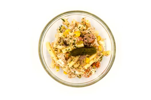 Pasta salad dish with corn, tuna and a pickle on a gray background