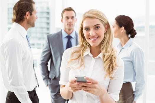 Businesswoman text messaging with colleagues in meeting behind at office