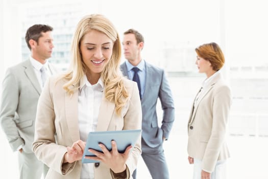 Portrait of businesswoman using digital tablet with colleagues behind in office