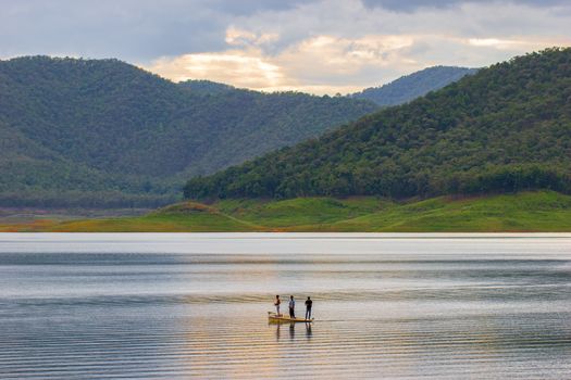 Three men standing on the boat and fishing in middle of the dam among mountain.