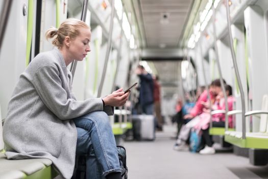 Portrait of lovely girl typing message on mobile phone in almost empty public subway train. Staying at home and social distancing recomented due to corona virus pandemic outbreak.