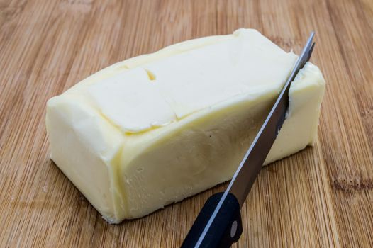 Rectangular clod of butter with a black knife on a wooden background