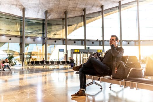 Casual young man talking on cell phone while waiting to board a plane at airport departure gates.