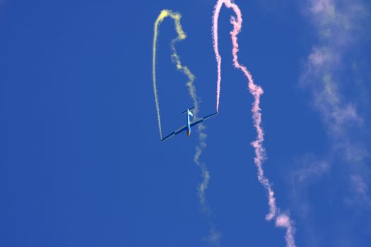 Glider performing aerobatics with smoke trails at airshow on sunny day in Switzerland