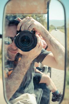 Israeli man reflected on the side mirror of an electric golf cart while taking a self portrait picture. He traveling in the countryside of Israeli Hula Valley in summer day. Close up and selective focus.