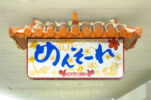 Japanese Okinawan Mensore sign which means Welcome decorated with a traditional house roof decorated with a lion Shisa in the Arrivals Hall of Naha Airport.