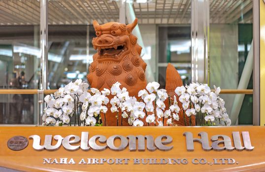 Japanese Okinawan lion Shisa sculpture decorated with white orchids flowers in the Welcome Hall of Naha Airport in the south of Okinawa Island.