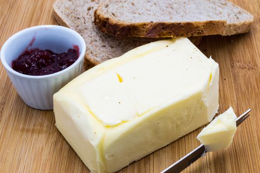 Block of fresh rectangular butter with jam and slices of bread