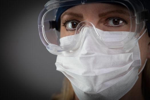 Female Medical Worker Wearing Protective Face Mask and Gear Against Dark Background.