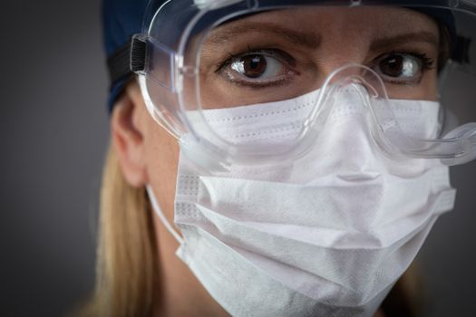 Female Medical Worker Wearing Protective Face Mask and Gear Against Dark Background.