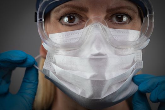 Female Medical Worker Wearing Protective Face Mask and Gear Against Dark Background.