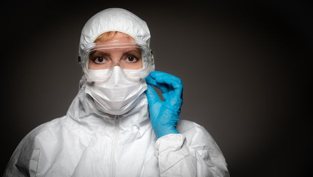 Female Medical Worker Wearing Protective Face Mask and Gear Against Dark Background.