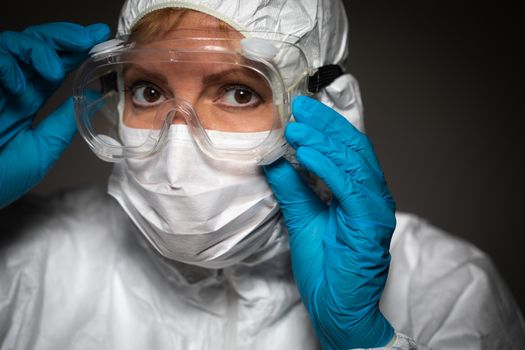 Female Medical Worker Wearing Protective Face Mask and Gear Against Dark Background.