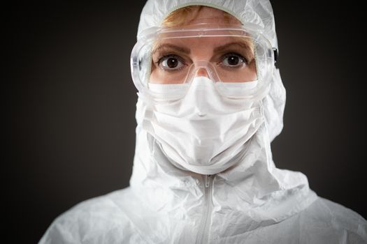 Female Medical Worker Wearing Protective Face Mask and Gear Against Dark Background.