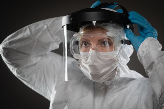Female Medical Worker Wearing Protective Face Mask and Gear Against Dark Background.