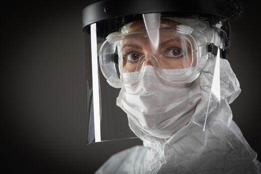 Female Medical Worker Wearing Protective Face Mask and Gear Against Dark Background.