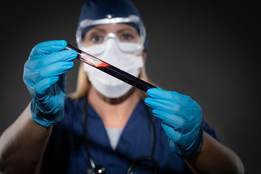 Female Lab Worker Wearing Medical Face Mask Holds Test Tube of Blood Against Dark Background.