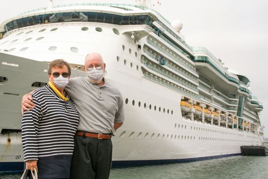 Senior Couple Wearing Face Masks Standing In Front of Passenger Cruise Ship.