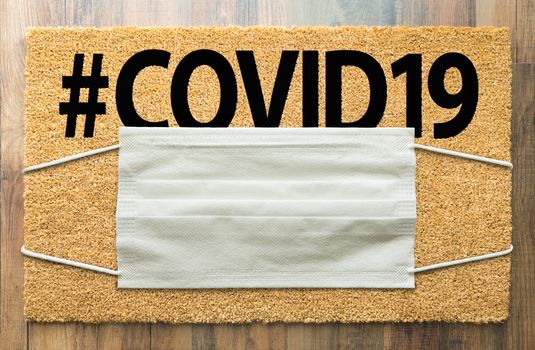 Welcome Mat With Medical Face Mask and #COVID19 Text Amidst The Coronavirus Pandemic.