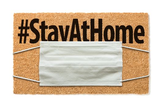 Welcome Mat With Medical Face Mask and #Stay At Home Text Isolated on White Amidst The Coronavirus Pandemic.
