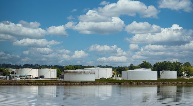 Old white storage tanks on the shore with relfections in water