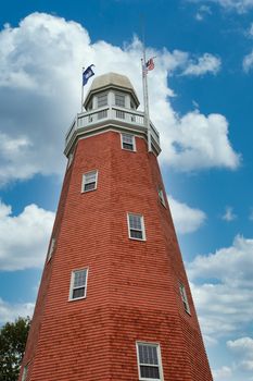 An old lighthouse covered with red shingles and white windows on a nice sky