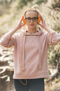 Portrait of beautiful sports woman wearing sunglasses, hoodie and headphones during outdoors training session. Healthy lifestyle image of young caucasian woman jogging outside.