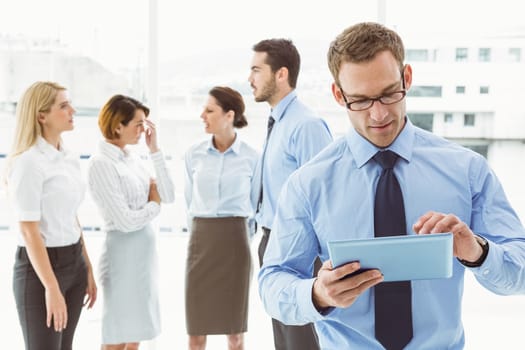 Businessman using digital tablet with colleagues behind in office