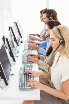 Side view of young business people with headsets using computers in office