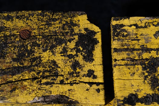 A part of old yellow wooden fence. The yellow paint on wood is old and cracked. Perfect painted wooden texture.