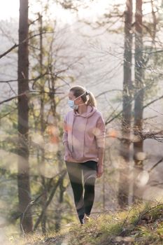 Portrait of caucasian sporty woman wearing a medical protection face mask while walking in the forest. Corona virus, or Covid-19, is spreading all over the world.