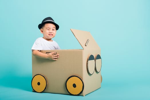 Happy Asian children boy smile in driving play car creative by a cardboard box imagination, summer holiday travel concept, studio shot on blue background with copy space for text