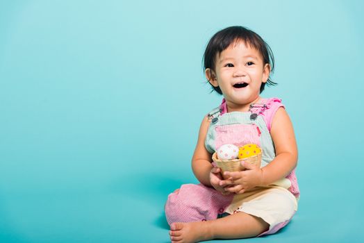 Asian Cute little baby girl beautiful holding Easter egg in basket, studio shot on blue background with copy space, Easter day concept