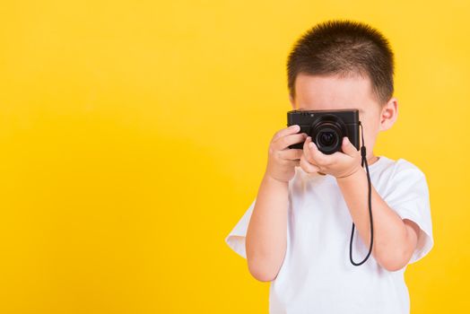Asian Thai happy portrait cute little cheerful child boy hold photo camera compact doing taking the picture, studio shot isolated on yellow background with copy space