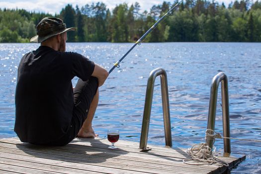 Mature man fishing from wooden pier near cottage on lake in Finland at summer