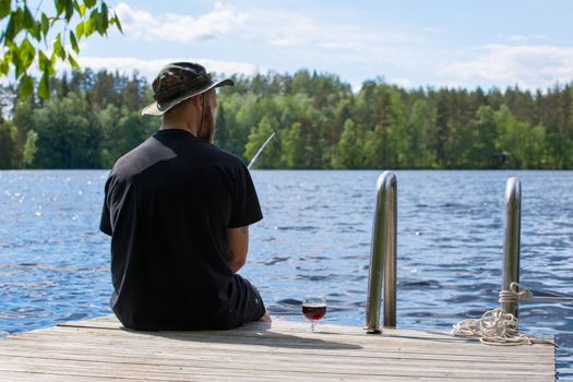 Mature man fishing from wooden pier near cottage on lake in Finland at summer