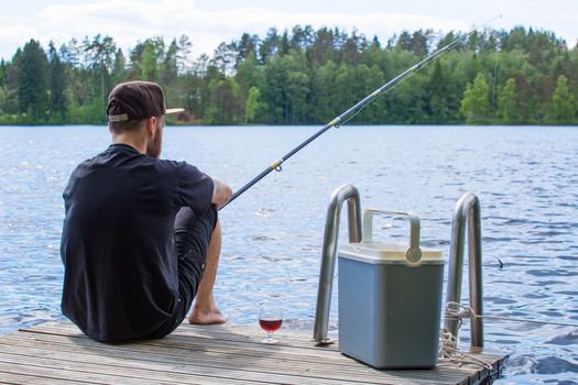 Mature man fishing from wooden pier near cottage on lake in Finland at summer