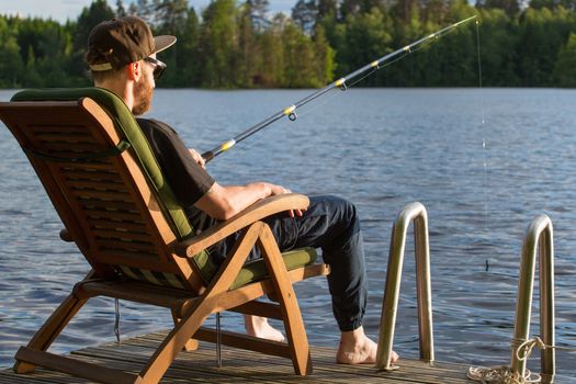 Mature man fishing from wooden pier near cottage on lake in Finland at summer