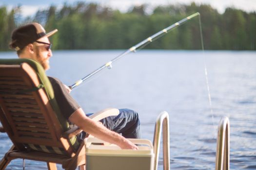 Mature man fishing from wooden pier near cottage on lake in Finland at summer