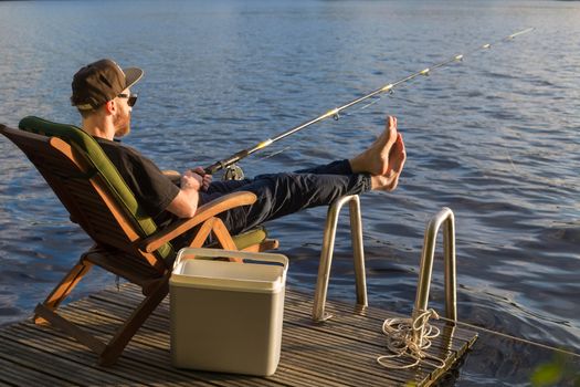 Mature man fishing from wooden pier near cottage on lake in Finland at summer