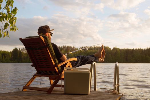 Mature man fishing from wooden pier near cottage on lake in Finland at summer