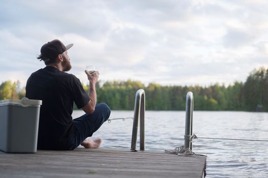 Mature man fishing from wooden pier near cottage on lake in Finland at summer