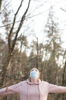 Portrait of caucasian sporty woman wearing medical protection face mask while relaxing by taking a deep breath in nature. Corona virus, or Covid-19, is spreading all over the world.