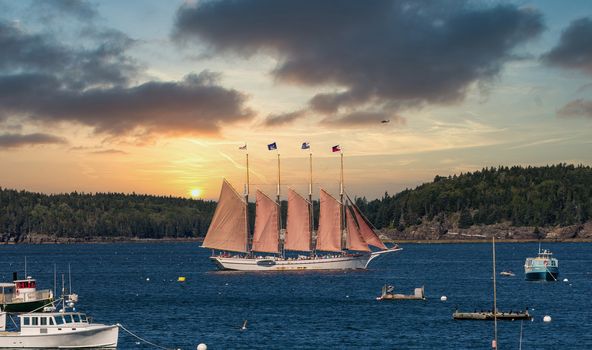 A four masted schooner touring sightseers through a blue harbor off Bar Harbor, Maine