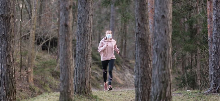 Portrait of caucasian sporty woman wearing a medical protection face mask while running in nature. Corona virus, or Covid-19, is spreading all over the world.