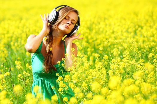 Young woman with headphones listening to music on oilseed flower field