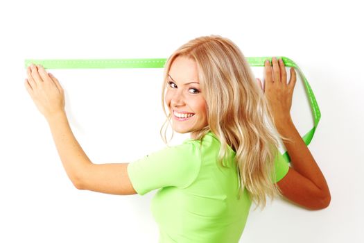 Young beautiful smiling woman measuring spacing on a wall with green measure tape, white background