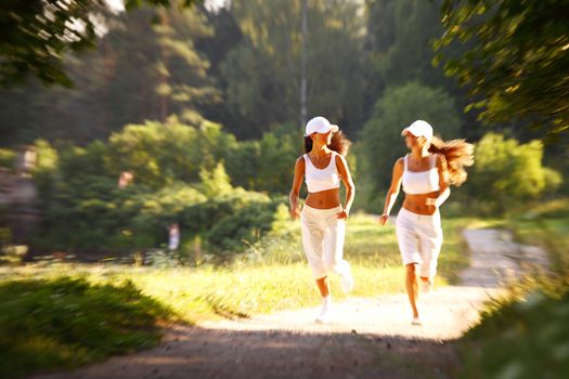 Two female runners run in summer park, women friends